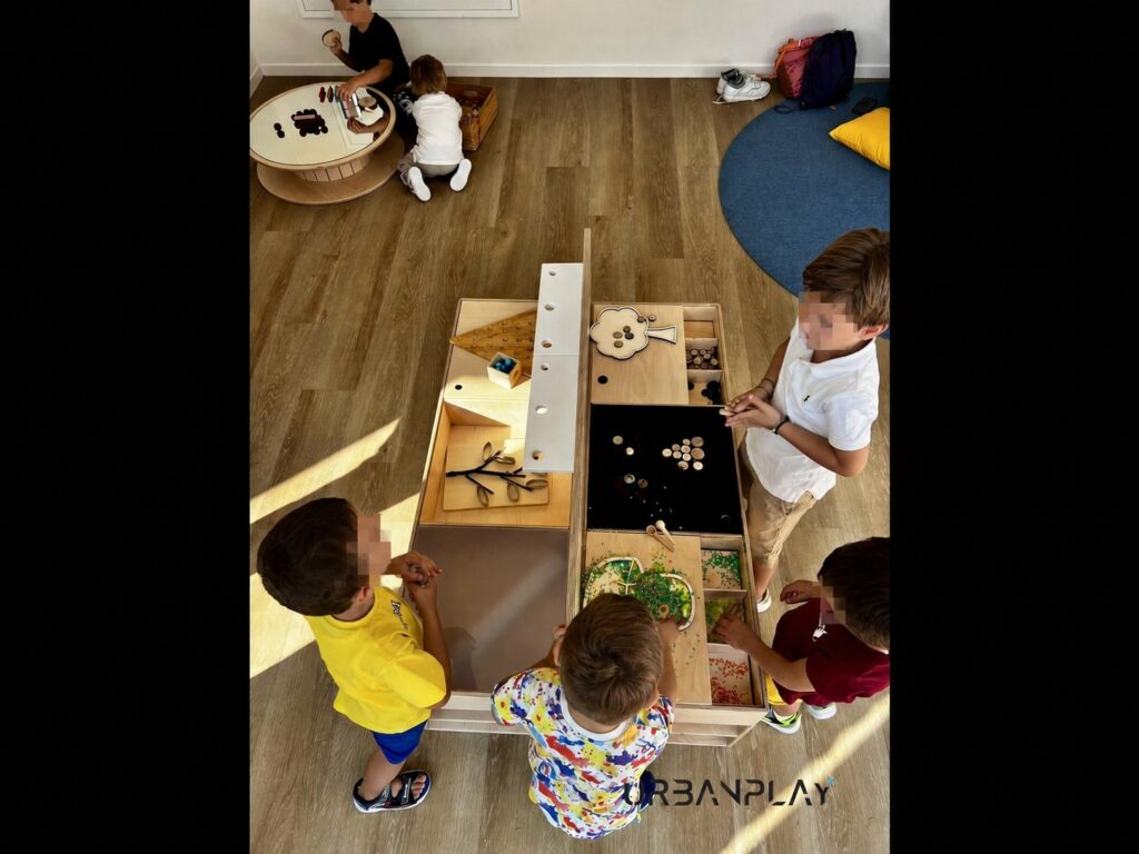 Bambini impegnati in attività sensoriali attorno a un tavolo educativo in legno