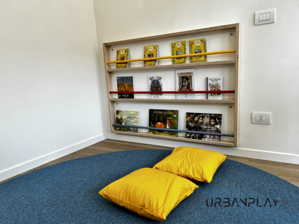 Angolo lettura con libreria frontale, tappeto e cuscini nello spazio infanzia