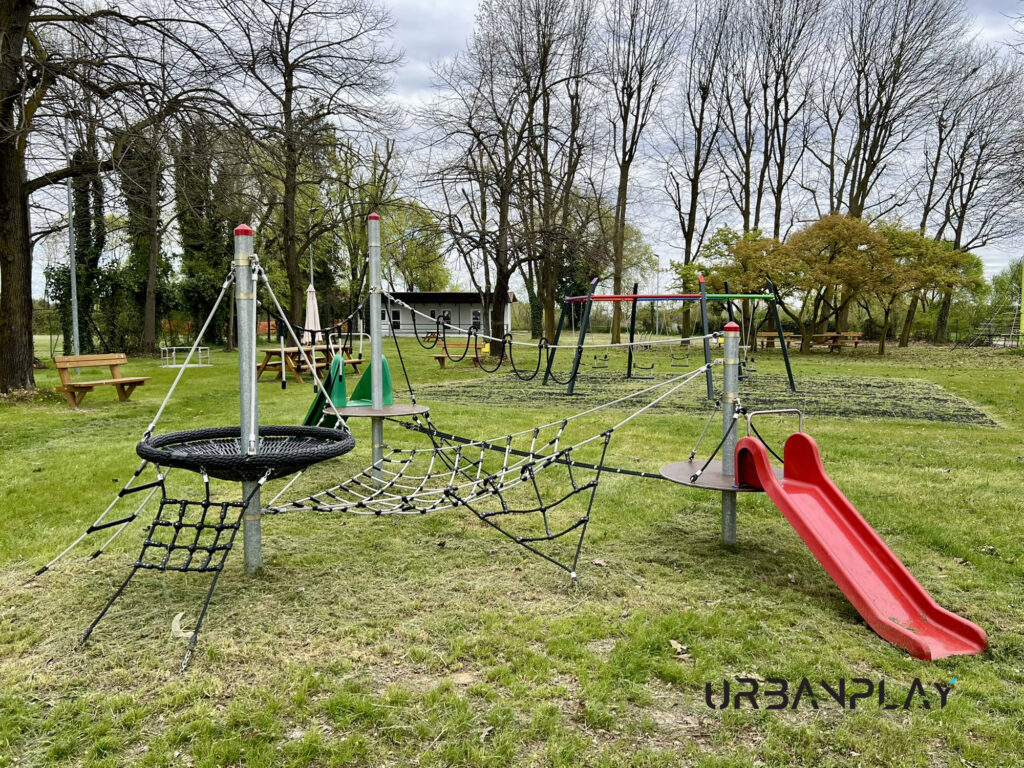 Rete di arrampicata piramidale nel parco giochi Verolengo con torre dell’acqua sullo sfondo
