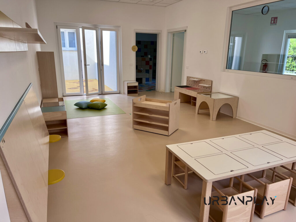 Ambiente educativo con tavolo attività, area morbida, contenitori e arredi gioco