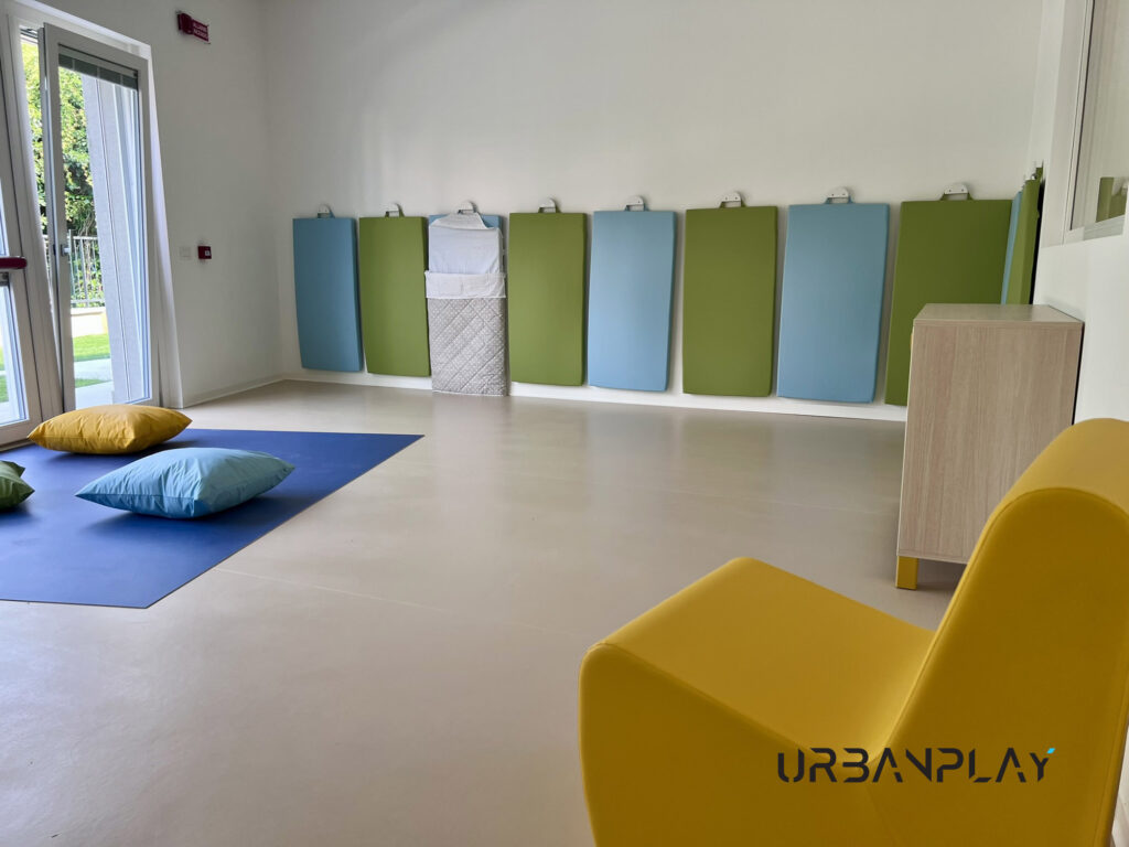 Zona relax con poltrona imbottita, tappeto morbido, cuscini e materassini a parete