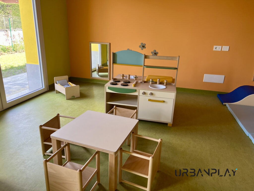 Area gioco simbolico per asilo nido con cucina in legno, tavolino e sedute per bambini